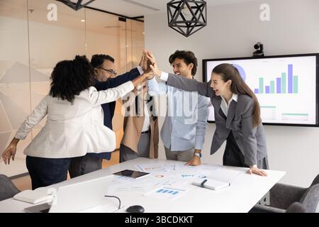Professionals giving high five gathered together around conference table Stock Photo