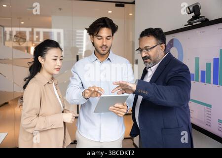 Teammates discussing data on tablet standing next to digital screen Stock Photo