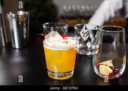 Classic whiskey sour cocktail in a lowball glass, garnished with a cherry and ice cube, set on a stylish black bar counter. Stock Photo
