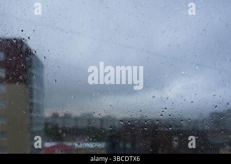 a raindrops on the window pane, clouds behind the glass, raining, city roofs behind the raindrops Stock Photo