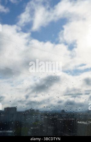 a raindrops on the window pane, clouds behind the glass, raining, city roofs behind the raindrops Stock Photo