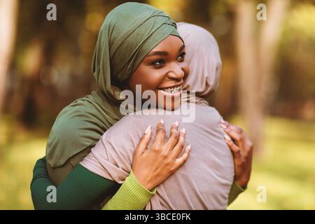 Two Diverse Islamic Ladies Embracing Standing In Park Outside Stock Photo