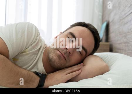 view of young man is sleeping in the bed. the guy enjoys sleeping on the background of the window in the morning. An interesting dream Stock Photo