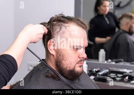 The hands of young barber making haircut to attractive man in barbershop Stock Photo