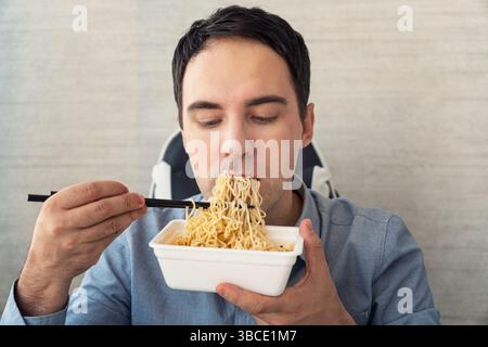 Young man eating instant noodles while working with in office. Lunch at the office. junk food Stock Photo