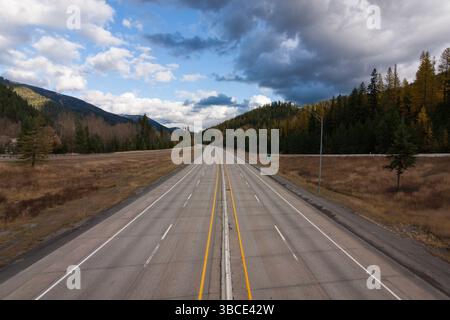 Empty highway stretching through forested mountains under a dramatic sky in the USA, evoking solitude and scenic American road travel. Stock Photo