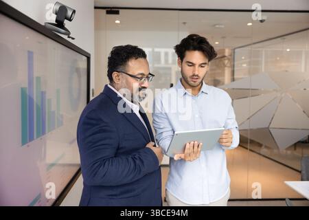 Two focused businessmen analyzing performance metrics displayed on tablet Stock Photo