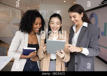 Three multiethnic businesswomen standing in office using digital tablet Stock Photo