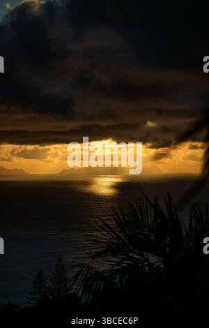 Dramatic sunset over the ocean with islands silhouetted against golden light and dark clouds Stock Photo
