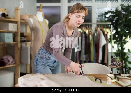 Female seamstress cutting fabric with scissors on worktable Stock Photo