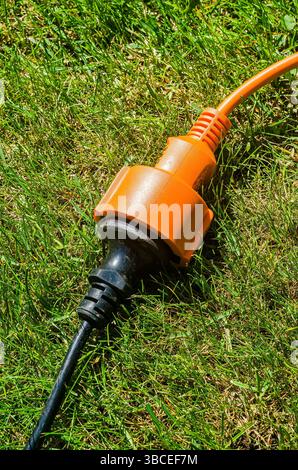 lectrical extension cord with orange plug resting on green grass for outdoor use. High quality photo Stock Photo