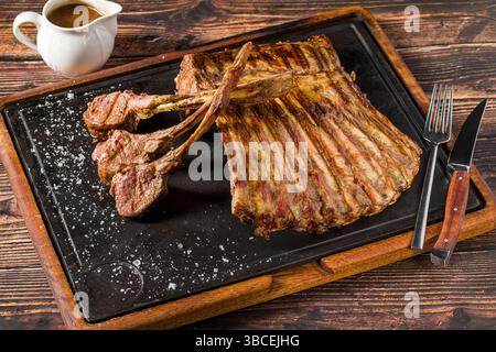 Lamb racks grilled with herbs and sauce on a stone board Stock Photo