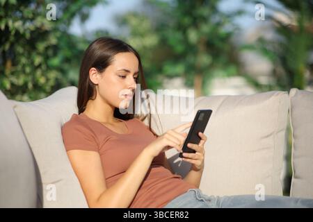Serius woman using mobile phone sitting in a garden at home Stock Photo
