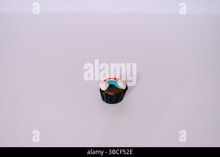 Rainbow decorated cupcake on a plain backdrop, perfect for birthday celebration or creative treat Stock Photo
