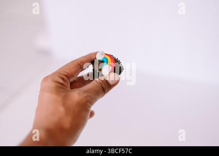 A person is holding a brownie bite decorated with a rainbow frosting detail. A simple and minimal shot on white background Stock Photo