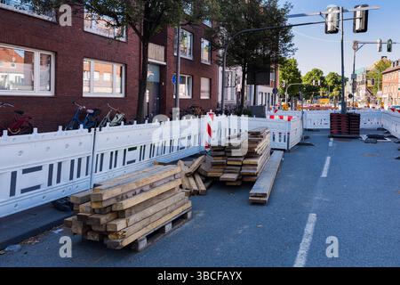 A construction site is visible with stacked wooden planks on the ground. Barriers line the street, while bicycles are parked nearby. Stock Photo