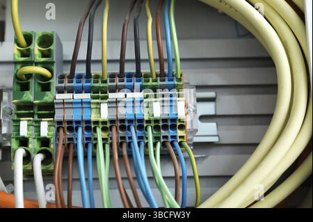many colorful electrical wires lead into a relay and transformer panel on a wall at an unfinished construction site Stock Photo