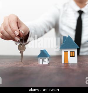 Businesswoman holding keys. olored paper houses standing on desk Stock Photo