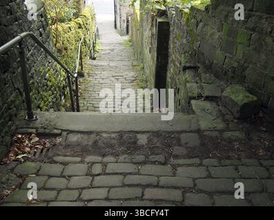 Old outdoor stone steps in dark alley with cobblestones and moss growing on the walls Stock Photo