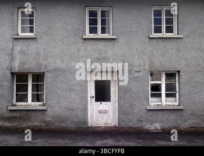 An old abandoned grey derelict house on a residential street with dirty broken windows Stock Photo