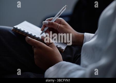 Close up on Black womans hands writing in notebook on laps keeping notes on speakers presentation while attending business conference in auditorium, c Stock Photo