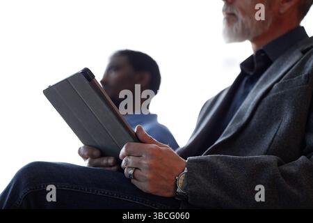 Close up on digital tablet in hands of mature male conference participant taking notes on device while listening to presenters speech in auditorium, c Stock Photo