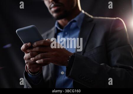Close up on smartphone in hands of Black male investor checking stock prices online monitoring finance performance in room with dim light, copy space Stock Photo