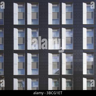 Facade of a large black and white modern commercial building with repeating windows and geometric panels Stock Photo