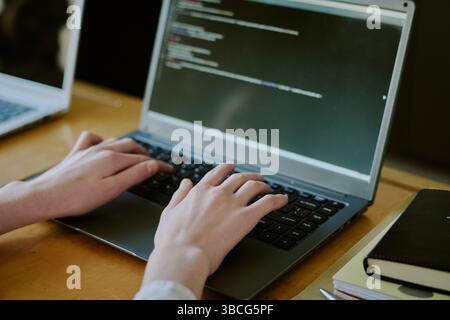 Close-up of hands typing code on laptop keyboard, with code visible on screen. Image focused on hands and coding activity, highlighting programming pr Stock Photo