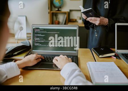 Students learning programming with a clergy member. Open laptops display code while notebooks lying on the desk, creating educational atmosphere Stock Photo