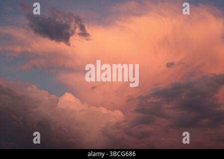 Dramatic pink and violet storm clouds illuminated by the setting sun, showing dynamic textures and moody atmosphere in the evening sky. Stock Photo