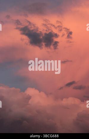 Dramatic pink and violet storm clouds illuminated by the setting sun, showing dynamic textures and moody atmosphere in the evening sky. Stock Photo