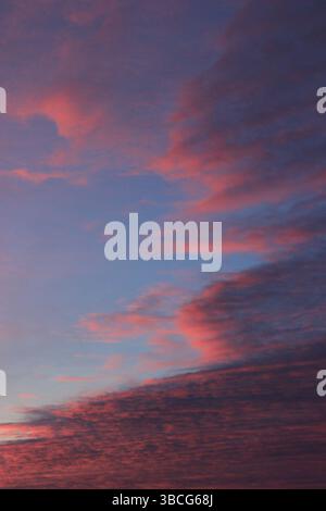 Layered crimson and violet clouds stretch across a twilight sky, creating a vivid and atmospheric sunset scene over the horizon. Stock Photo
