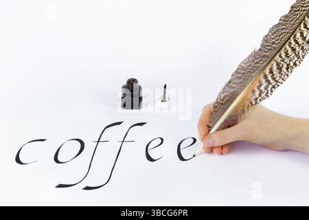 Hand holding bird feather writing the word coffee with black ink on white paper Stock Photo
