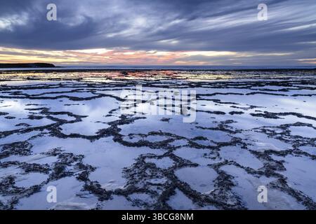 A beautiful sunset over the ocean with rocky beach and tidal pools in the foreground Stock Photo