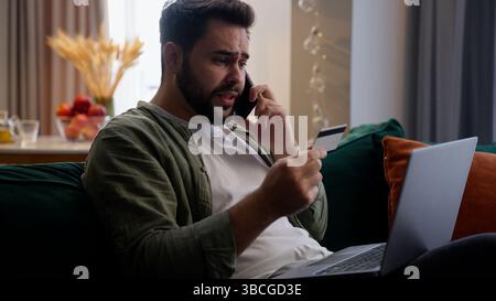 Nervous Caucasian business man male irritated annoyed guy client businessman freelancer entrepreneur talk mobile phone holding credit card transaction Stock Photo