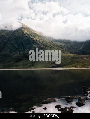 Lough Callee presents a serene view with calm waters reflecting green mountains and clouds in the early morning. Nature's beauty unfolds in a peaceful Stock Photo
