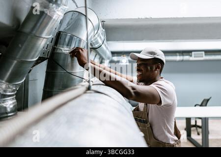 Worker performs maintenance on ductwork in a commercial building during daylight hours Stock Photo