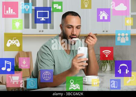Internet addicted man using mobile phone while eating at home. Different icons around him Stock Photo