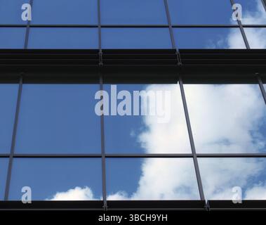 Clouds and bright blue sky reflected in the square mirrored windows of a modern commercial office building Stock Photo