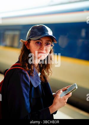 Woman in a cap using a smartphone beside a train at a station. Stock Photo