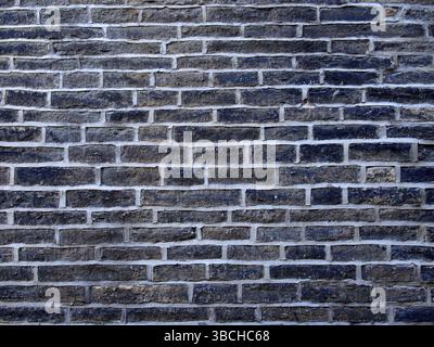 An old wall made of black stone bricks with grey cement Stock Photo