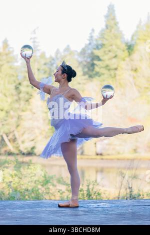 Ballerina in white tutu balancing on one leg with glass balls in an outdoor setting. WA, USA Stock Photo