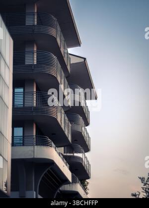 Contemporary hotel facade featuring sleek balconies and large glass windows, reflecting the sky in soft evening light. Clean lines and modern architec Stock Photo