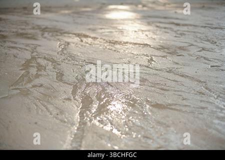 Wet sand with intricate patterns created by receding water reflecting sunlight. Thailand Stock Photo
