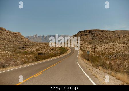 A long winding road stretches through a desert landscape with distant mountains under clear skies. Road Trip USA Stock Photo