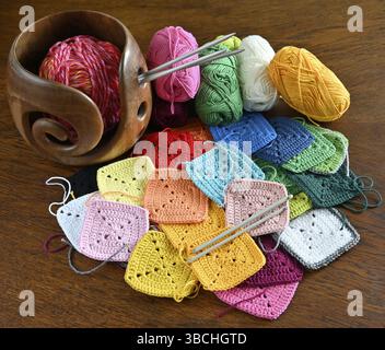 Colorful knitted squares, skeins of wool and a wooden yarn bowl for wool Stock Photo