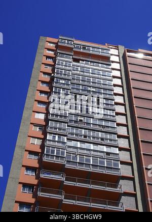 Vertical angled view of a tall concrete apartment block with balconies against a blue sky Stock Photo