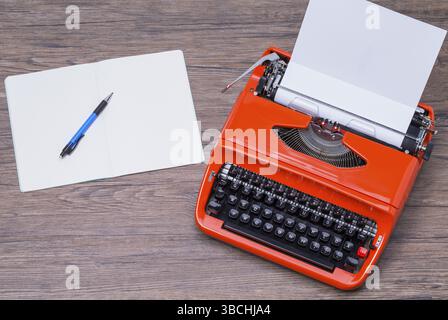 The photo shows a typewriter and a notebook on a wooden table Stock Photo