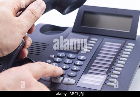 Photo shows a hand operating a telephone against a white background Stock Photo